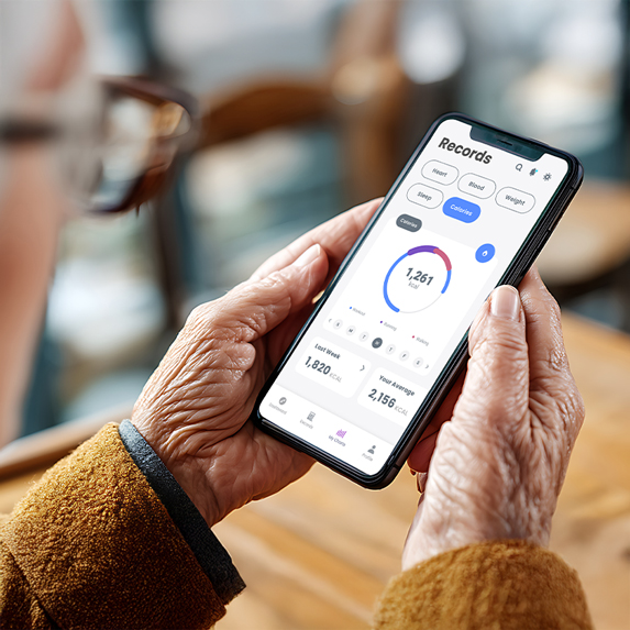 An older adult wearing glasses and a brown coat is holding a smartphone in both hands. The phone screen displays their health information. The background is softly blurred.
