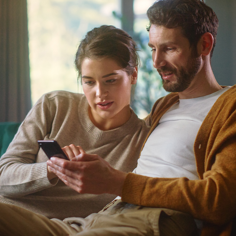 A couple sitting closely together looking at a phone together.